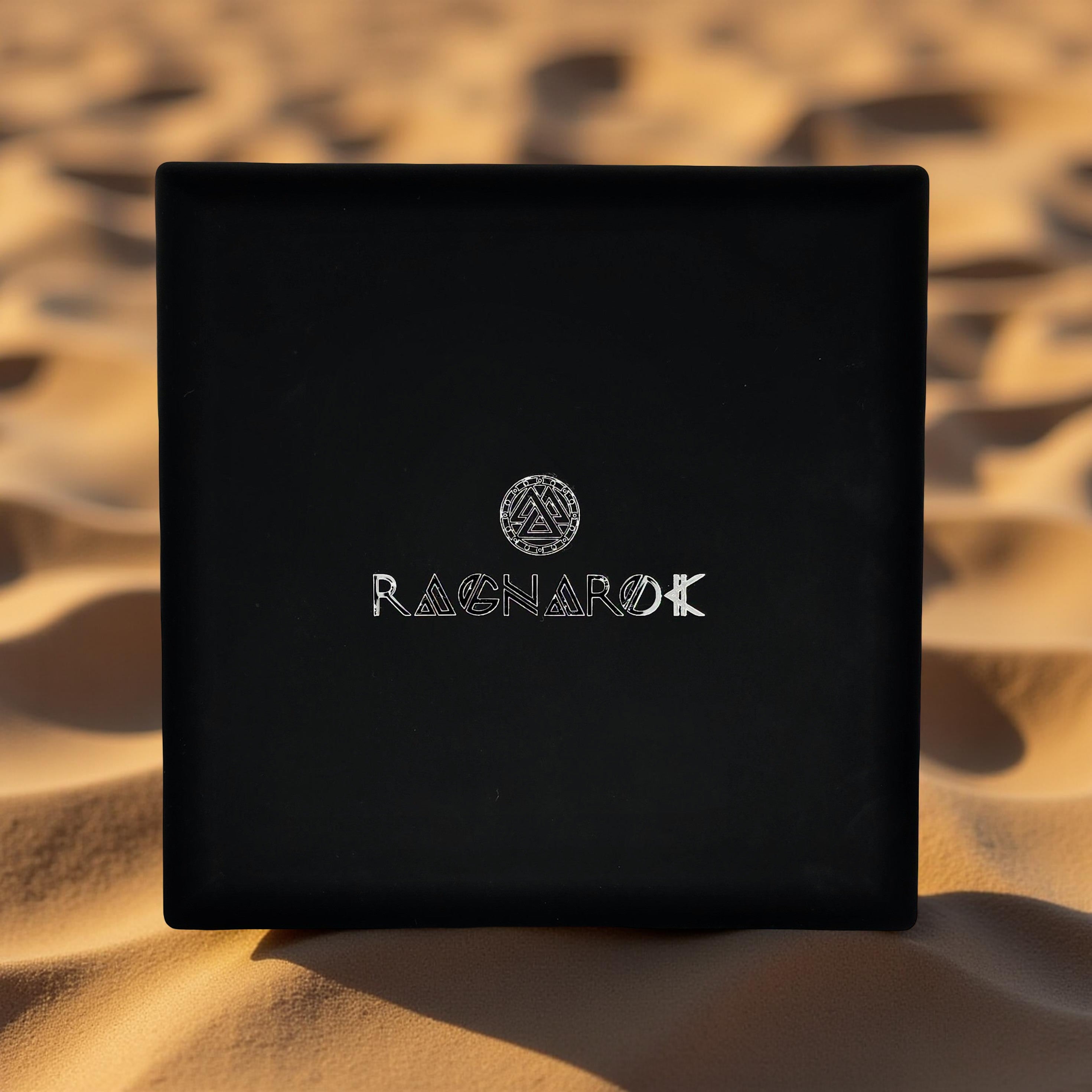 Black Ragnarok Jewelry & Apparel box with a silver logo, resting on golden desert sand dunes.