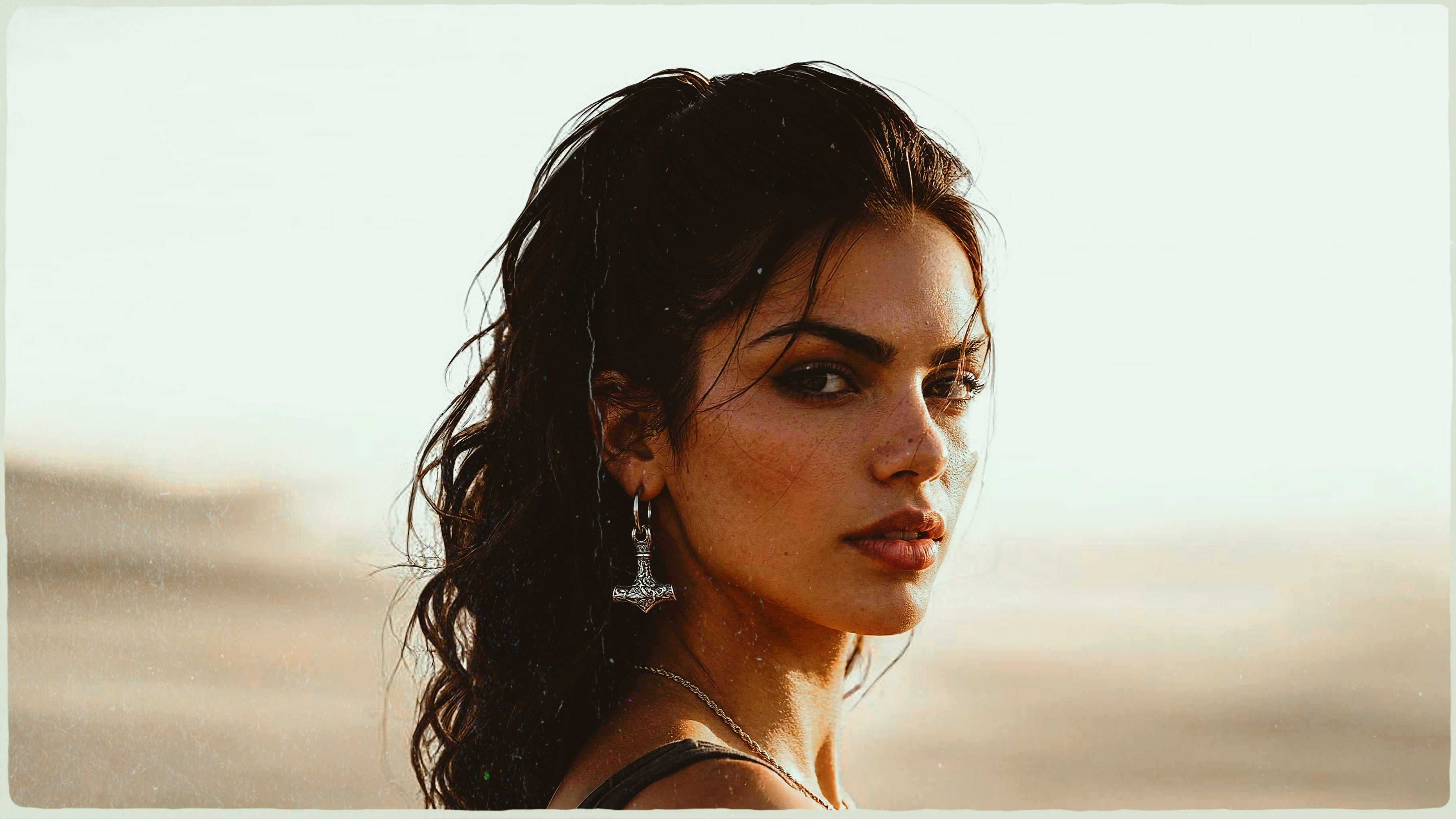 Dark-haired woman wearing a silver Mjolnir (Thor's hammer) earring and necklace, looking over her shoulder.