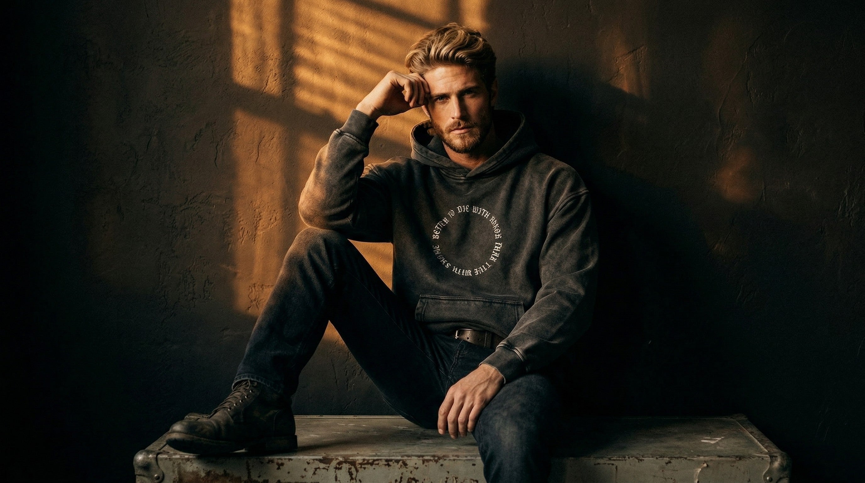 Man in a dark gray Ragnarok hoodie and jeans, sitting in warm window light.